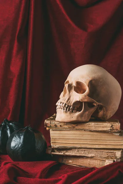 Halloween skull on ancient books with black pumpkins on red cloth — Stock Photo