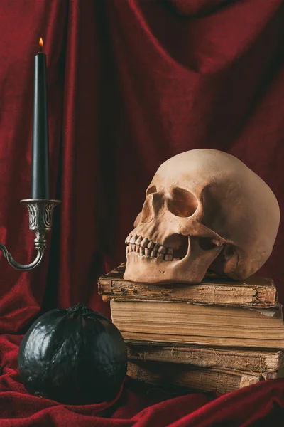 Halloween skull on ancient books with black pumpkin and candle on red cloth — Stock Photo