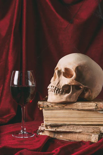 Calavera de halloween en libros antiguos con vino en tela roja - foto de stock