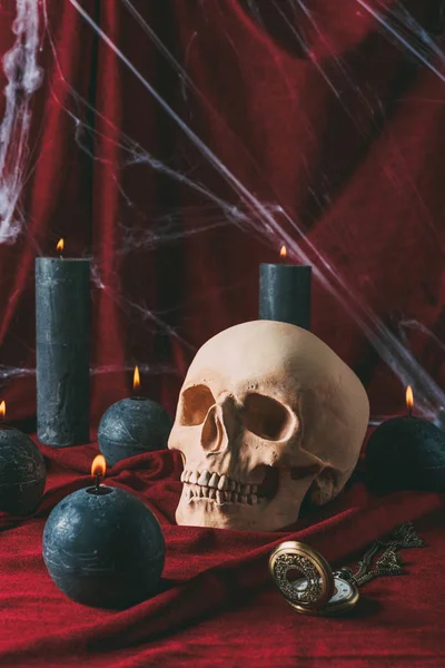 Cráneo, reloj vintage y velas negras en tela roja con tela de araña para halloween - foto de stock