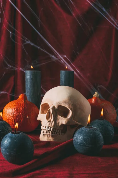 Spooky skull, pumpkins and black candles on black cloth with spider web, halloween decorations — Stock Photo