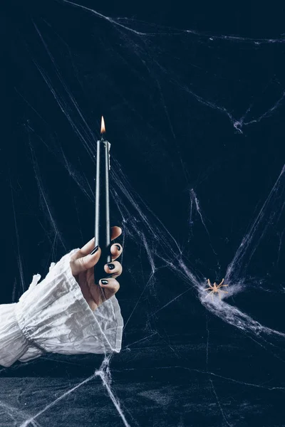 Partial view of creepy woman holding black candle in darkness with spider web — Stock Photo