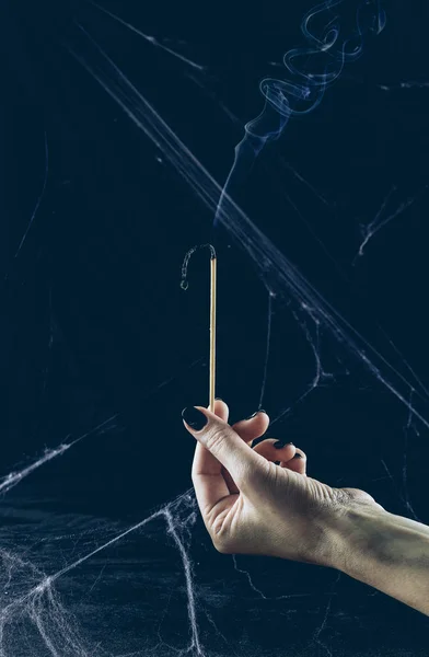 Partial view of gloomy woman holding big match with smoke in darkness with spider web — Stock Photo