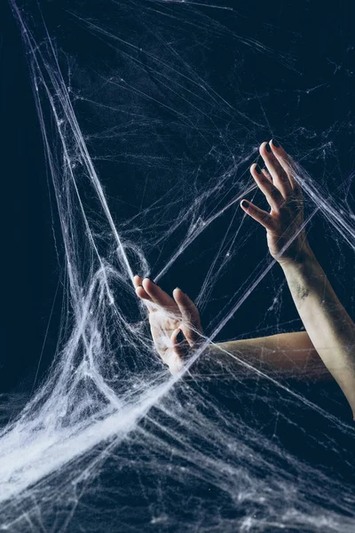 Cropped view of gothic woman with hands in spider web in darkness — Stock Photo