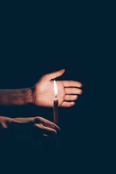 Vista cortada de pessoa segurando vela flamejante em mãos isoladas em preto — Fotografia de Stock