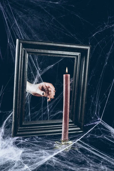 Cropped view of mystic hand taking candle from mirror frame with scary spider web around — Stock Photo