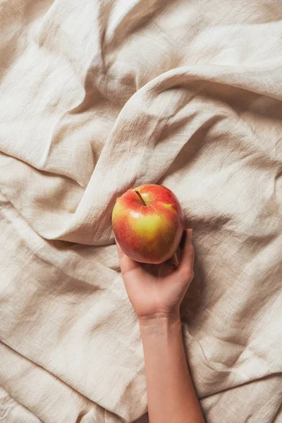 Cropped view of woman holding apple on beige sacking cloth — Stock Photo
