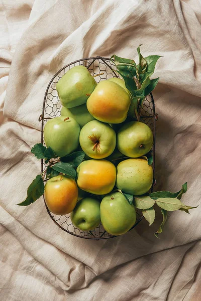 Зеленые яблоки в металлической корзине на мешковатой ткани — стоковое фото