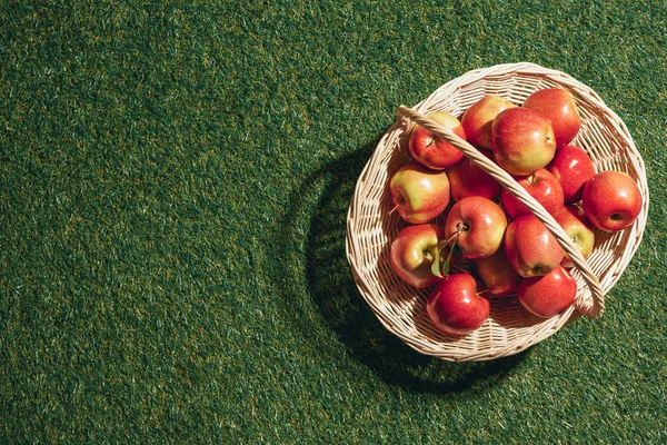Rote Äpfel in Weidenkorb auf Gras Hintergrund — Stockfoto