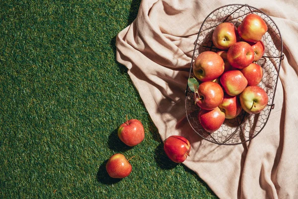 Pommes rouges dans un panier en métal sur toile de sac et herbe verte — Photo de stock