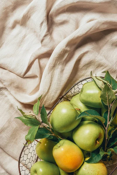 Вид сверху на зеленые яблоки в металлической корзине на мешковатой ткани — стоковое фото