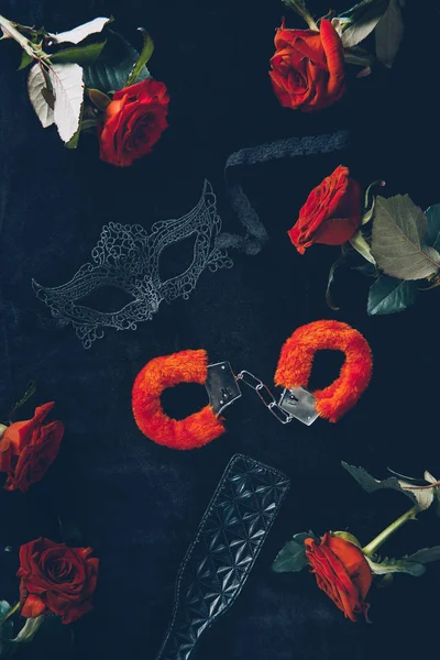 Вид зверху червоні пухнасті наручники, чорна мереживна маска, шкіряна прогулянкова весло та троянди — стокове фото