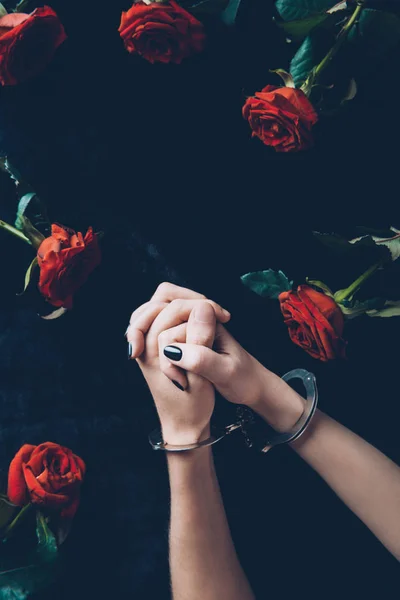 Plan recadré de femme menottée au-dessus du tissu noir avec des roses rouges — Photo de stock