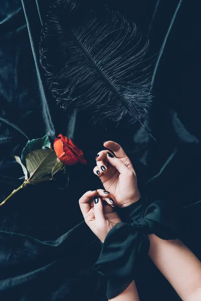 Cropped shot of woman with tied hands and red rose flower with black feather on fabric — Stock Photo