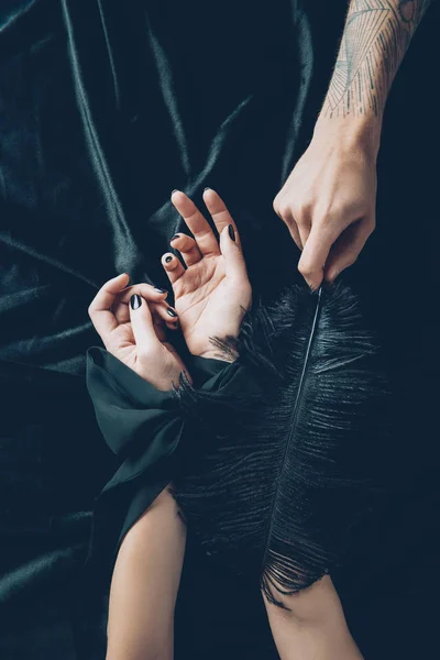 Cropped shot of woman with tied hands and man holding black feather — Stock Photo