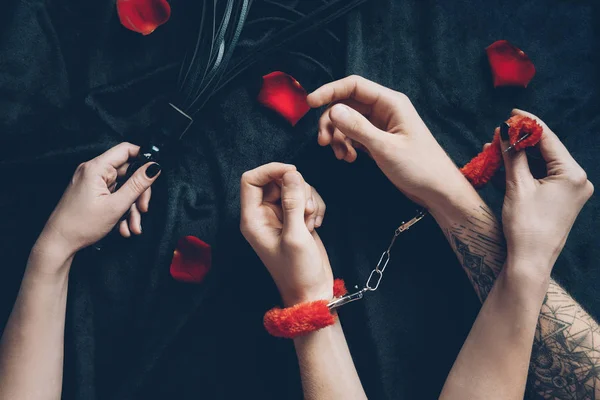 Partial view of couple in red fluffy handcuffs holding black leather whip — Stock Photo