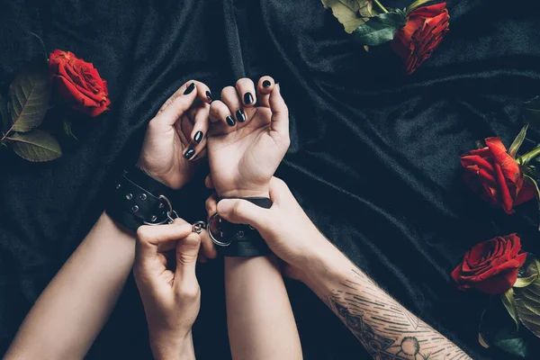 Cropped shot of couple in erotic game with black leather handcuffs — Stock Photo