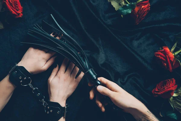 Ritagliato colpo di uomo in possesso di frusta nera e donna in manette di pelle — Foto stock