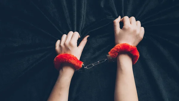 Cropped shot of woman in red fluffy handcuffs holding black fabric — Stock Photo