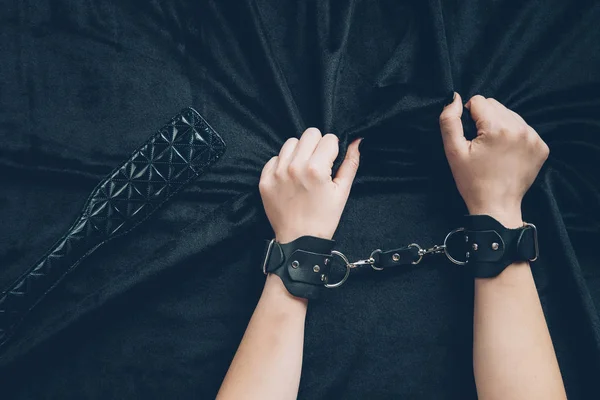 Cropped shot of woman in leather handcuffs holding black fabric — Stock Photo