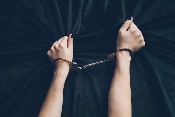 Cropped shot of female hands in handcuffs holding black fabric — Stock Photo