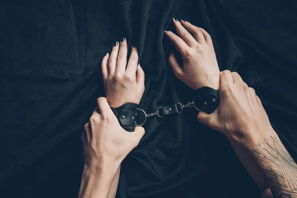 Partial view of man holding hands of partner in leather handcuffs — Stock Photo