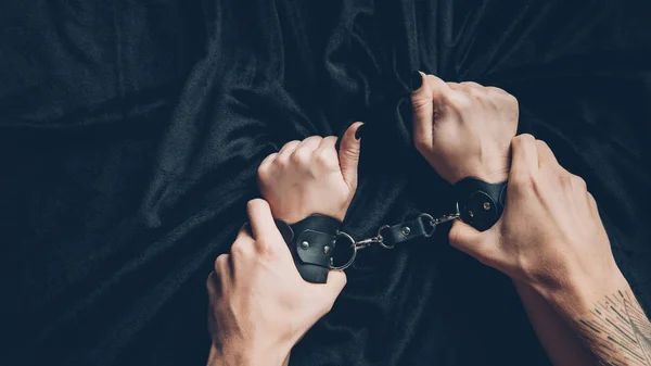 Cropped shot of man holding hands of partner in leather handcuffs — Stock Photo