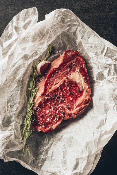 Vista superior de carne crua bife e alecrim sobre papel manteiga na cozinha — Fotografia de Stock