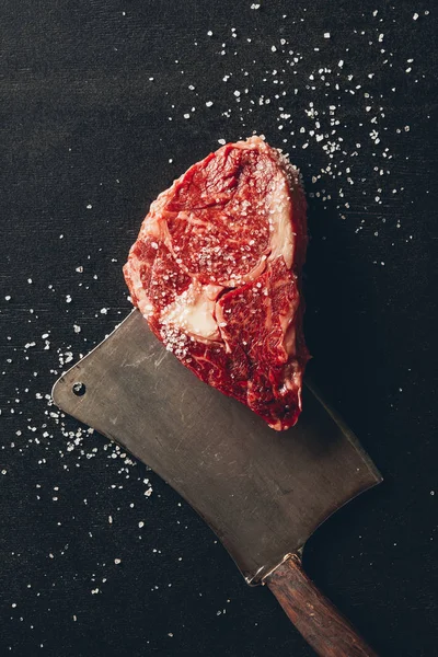 Top view of raw meat steak, salt and cleaver on tabletop in kitchen — Stock Photo