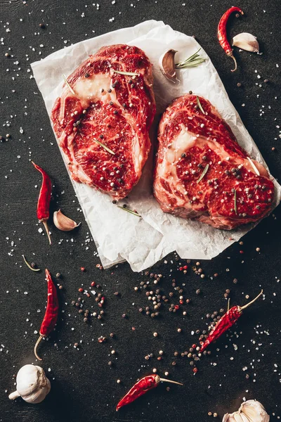 Elevated view of raw steaks, baking paper and scattered spices on table in kitchen — Stock Photo