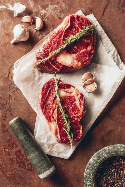 Top view of two uncooked steaks, pestle, mortar and spices on surface in kitchen — Stock Photo