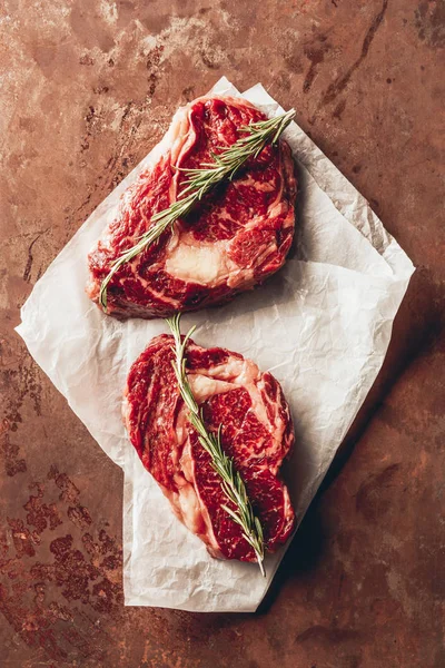 Vue de dessus de deux steaks crus avec romarin sur papier cuisson dans la cuisine — Photo de stock