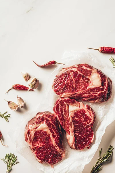 Vista superior de tres trozos de filetes de carne cruda y verduras sobre papel de hornear en la cocina — Stock Photo