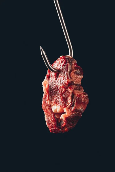 Morceau de viande crue accroché sur crochet métallique isolé sur noir — Photo de stock