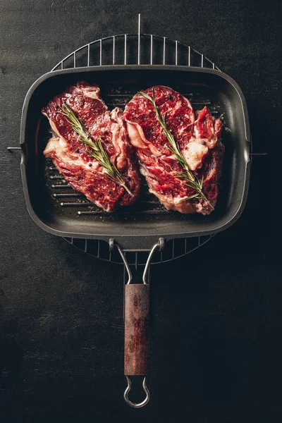 Erhöhte Sicht auf ungekochte Steaks mit Rosmarin auf Grillpfanne in der Küche — Stockfoto
