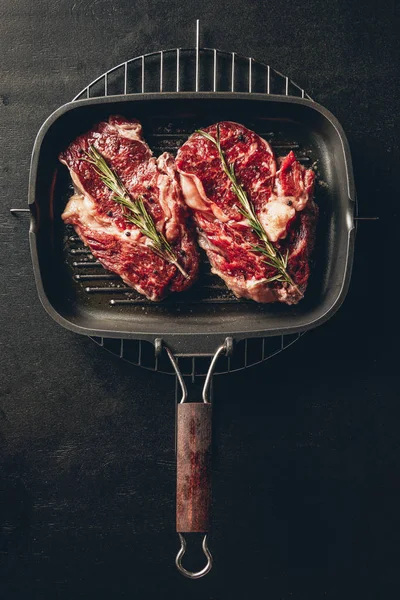 Vista elevada de bifes não cozidos com alecrim na grelha na cozinha — Fotografia de Stock