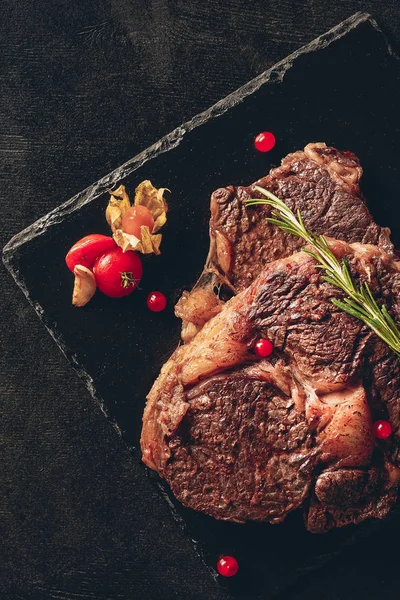 Elevated view of appetizing steaks with rosemary and berries on cutting boards in kitchen — Stock Photo