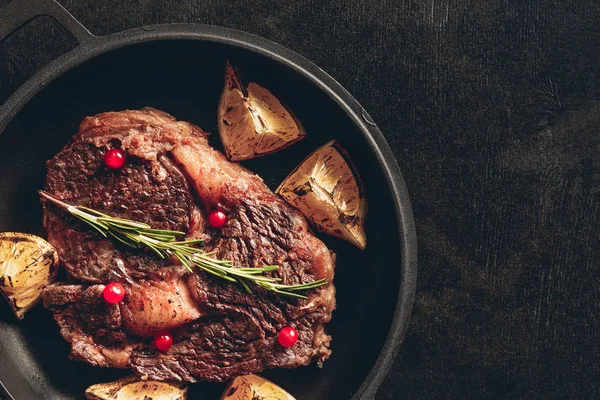 Top view of cooked steak with rosemary, lemons and berries on frying pan in kitchen — Stock Photo