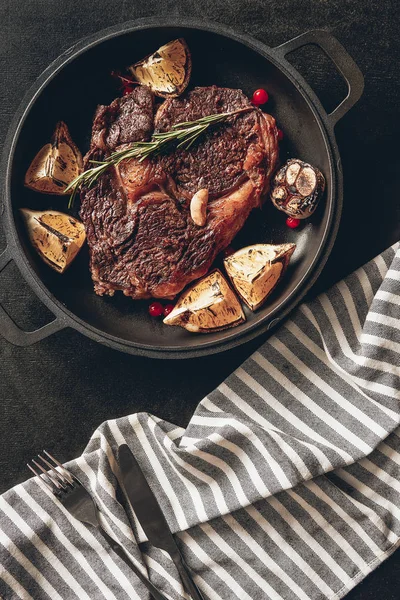 Elevated view of cooked steak with lemons and berries on frying pan, striped tablecloth on surface in kitchen — Stock Photo
