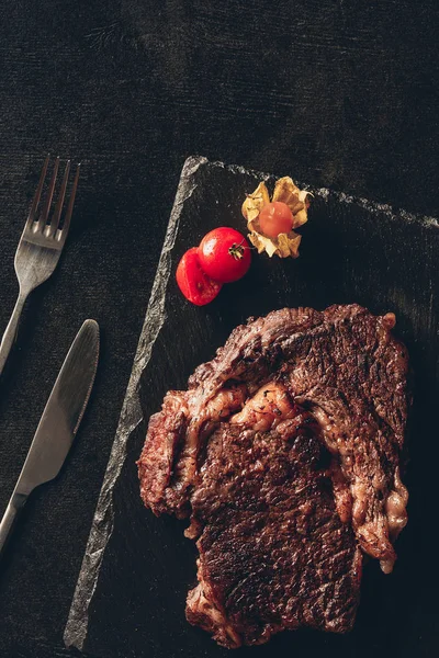 Vista sopraelevata di bistecca arrosto e bacca sul tagliere nero, coltello e forchetta sul tavolo in cucina — Foto stock