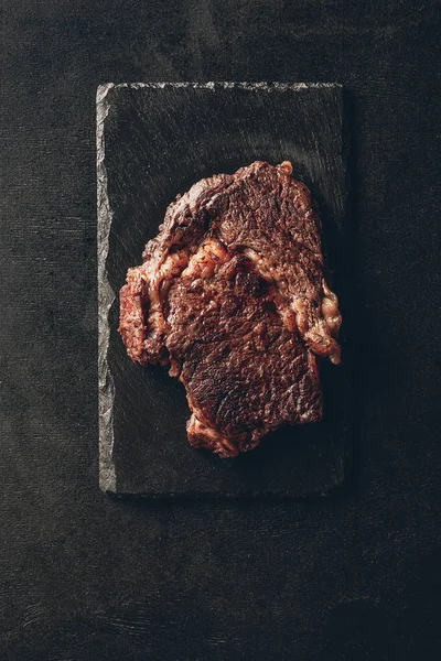 Vista superior de bife assado na placa de madeira preta na cozinha — Fotografia de Stock