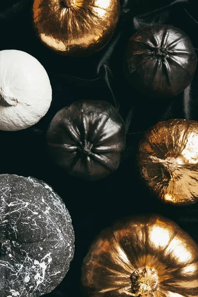 Верхний вид декоративных золотых, черно-белых окрашенных тыкв на черной ткани, дизайн Хэллоуина — стоковое фото