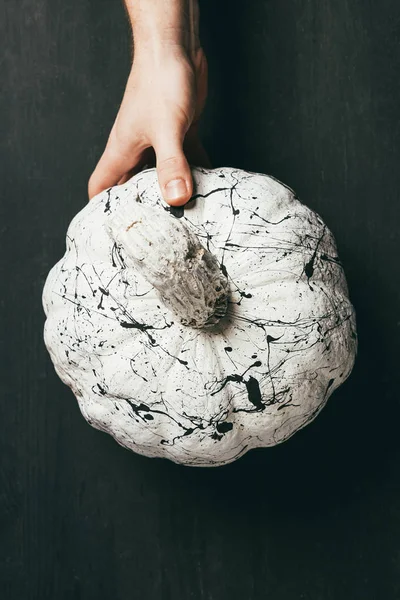 Teilansicht einer Person mit weißem Kürbis und schwarzen Farbspritzern, Halloween-Dekor — Stockfoto