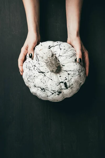 Cropped view of woman holding white pumpkin with black paint splatters, halloween decor — Stock Photo