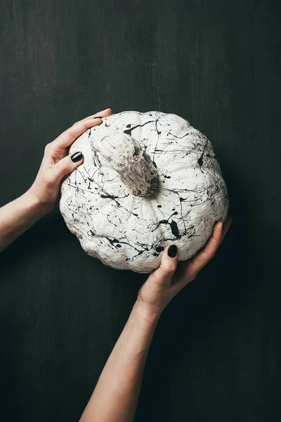 Cropped view of female hands holding white pumpkin with black paint splatters, halloween decoration — Stock Photo