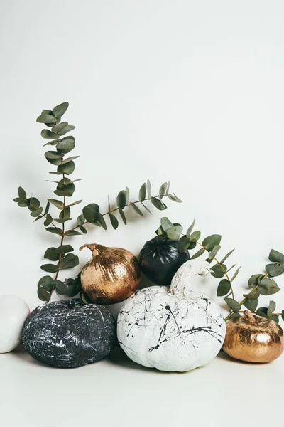 Nature morte avec des citrouilles dorées, noires et blanches avec éclaboussures de peinture et eucalyptus sur blanc — Photo de stock