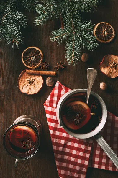 Blick von oben auf den traditionellen Weihnachtsglühwein mit Gewürzen auf hölzernem Hintergrund mit Tannenzweigen — Stockfoto