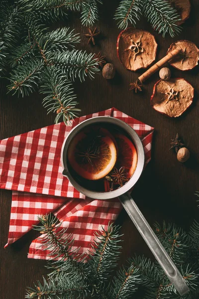 Top view of traditional christmas hot spiced wine on wooden background with dried apple slices and pine branches — Stock Photo