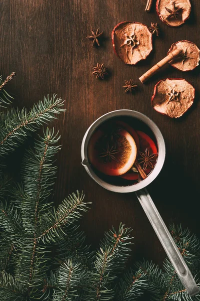 Blick von oben auf den traditionellen Weihnachtsglühwein mit Gewürzen auf hölzernem Hintergrund mit Tannenzweigen — Stockfoto