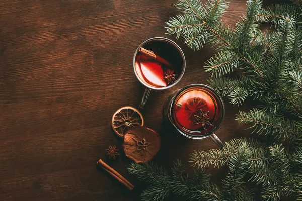 Vista superior de copas de vidrio con vino caliente casero condimentado sobre fondo de madera con ramas de abeto, bebida tradicional de Navidad - foto de stock